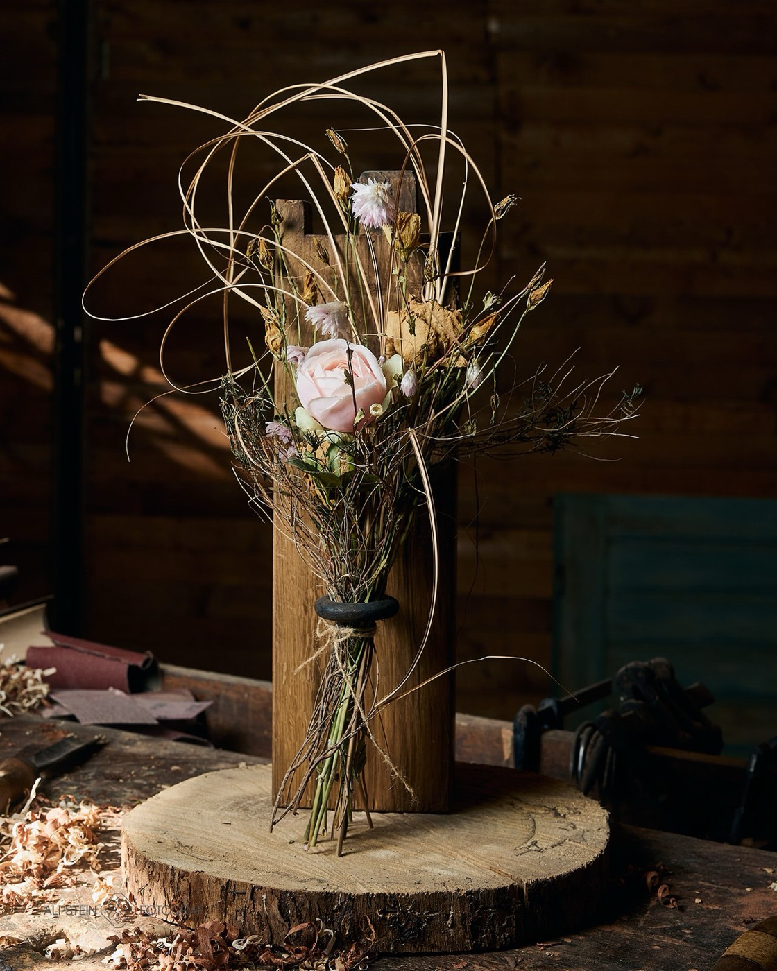 Blumenhalter aus altem Eichenbalken mit Trockenstrauss und rosa Rose auf einer Baumscheibe